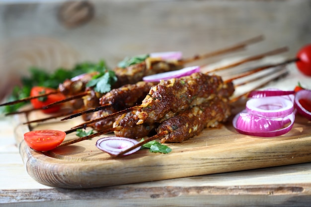 Appetizing lula kebab on wooden sticks with onion rings and herbs