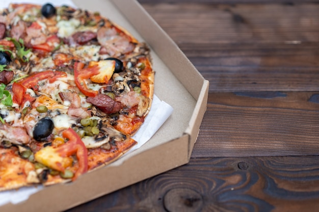 Appetizing pizza with smoked sausages bacon meat tomato cheese arugula cardboard boxes for delivery on black dark . With copyspace 