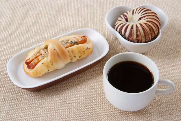 Appetizing sausage taro bread and cup of coffee on a fabric background