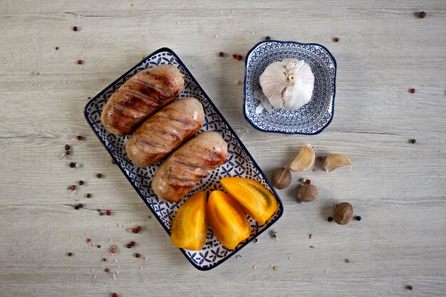 Appetizing sausages on blue plate with garlic and spices on a wood background