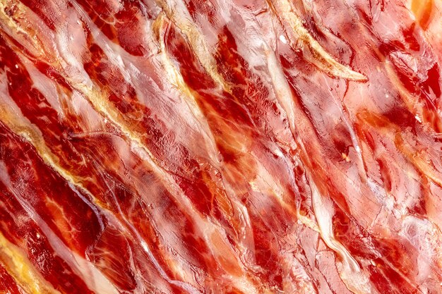 Appetizing slices Iberian ham in the foreground as a texture. Raw meat that becomes an article of haute cuisine and gastronomic luxury, through a process of raw salting and natural curing.