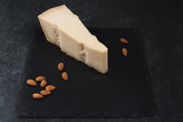 An appetizing solid cheese on a black plate with almonds