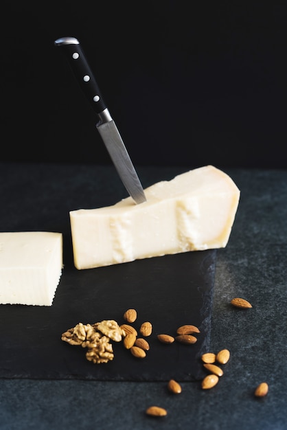 An appetizing solid cheese on a black plate with knife, almonds and nuts