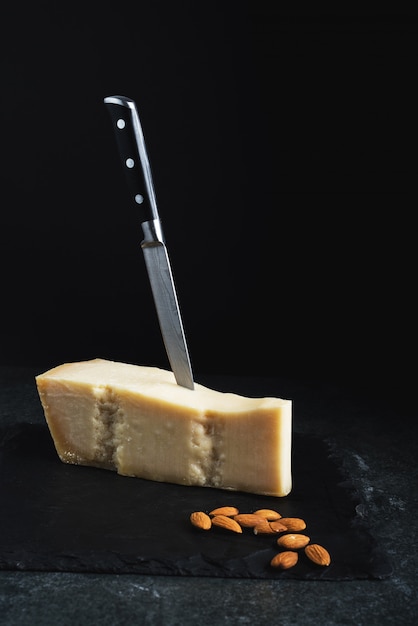 An appetizing solid cheese on a black plate with knife and almonds