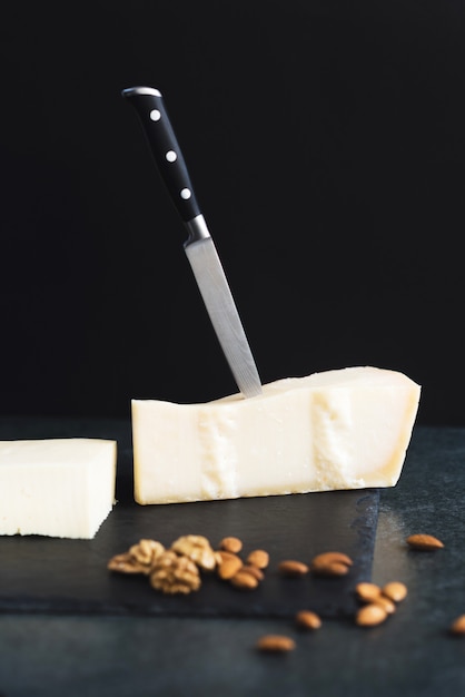 An appetizing solid cheese on a black plate with knife