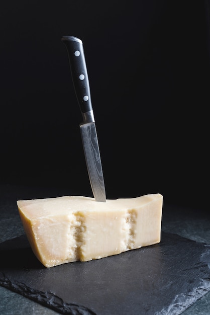 An appetizing solid cheese on a black plate with knife