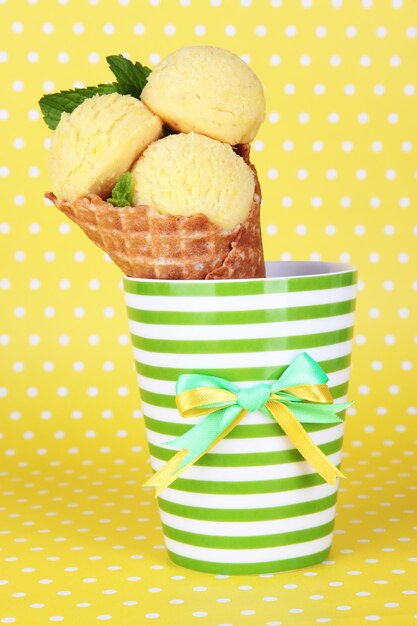 Appetizing yellow ice cream with waffle cone in cup on polka dot background