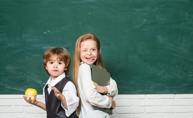 Apple and books school concept Girl and boy with happy face expression near desk with school supplie