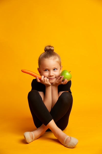 An apple, carrot and sports girl on a yellow background. Dieting and healthy eating concept