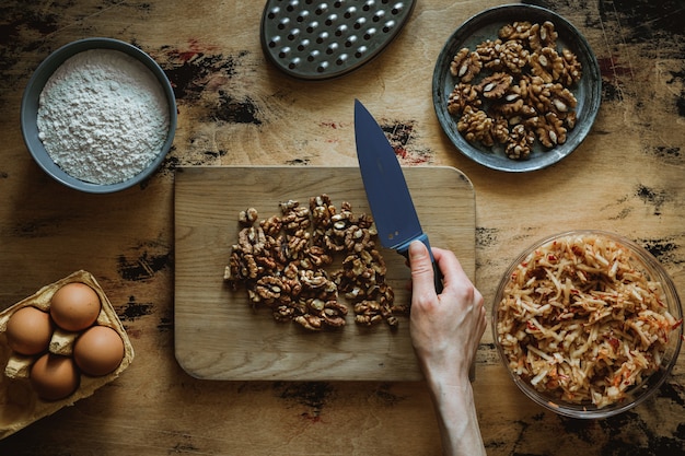 Apple carrot walnut loaf cake recipe. Chopping walnuts on a wooden chopping board with a knife.