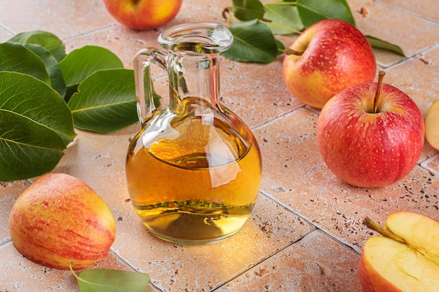 Apple cider vinegar of fermented fruit in glass bottle with apples on beige travertine tiles table background