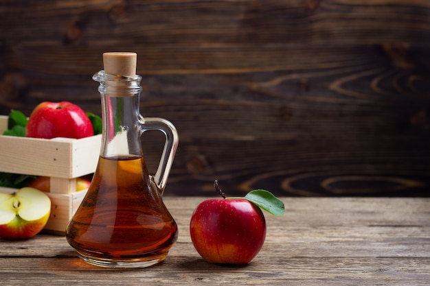 Apple cider vinegar and fresh red apple on a wooden background