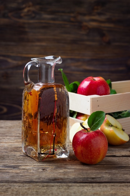 Apple cider vinegar and fresh red apple on a wooden background