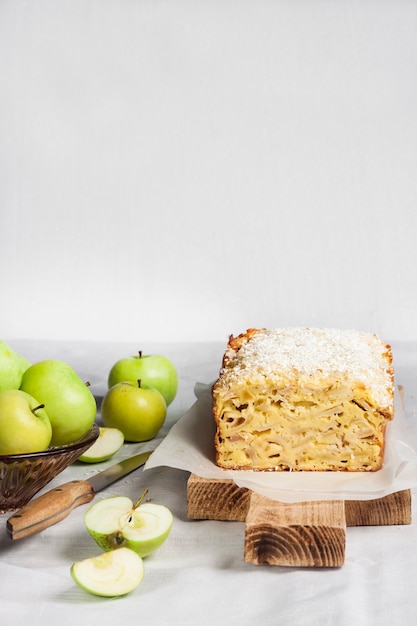 Photo apple and coconut oaf cake on wooden cutting board and apples in a vase. copy space