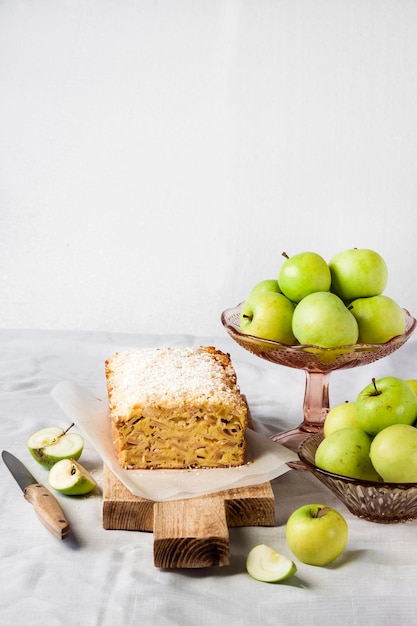 Apple and coconut oaf cake on wooden cutting board and apples in a vase. Copy space