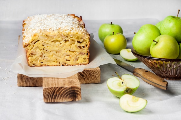 Apple and coconut oaf cake on wooden cutting board and apples in a vase