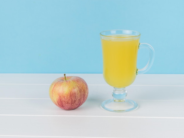 An apple and a glass of juice on a white wooden table