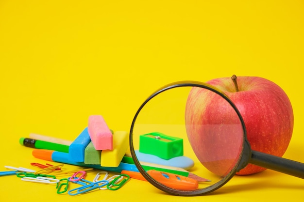 Apple magnifying glass and school stationery yellow background