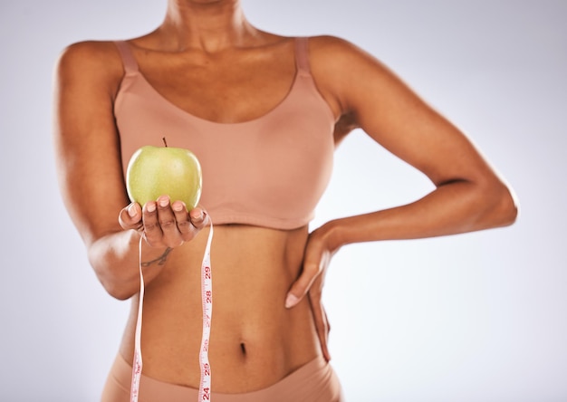 Photo apple measuring tape and diet with a black woman in studio on a gray background for weightloss food fitness and health with a female posing to promote exercise nutrition or health eating