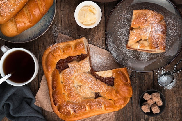 Apple pie, fresh rolls and tea on a brown wooden background.