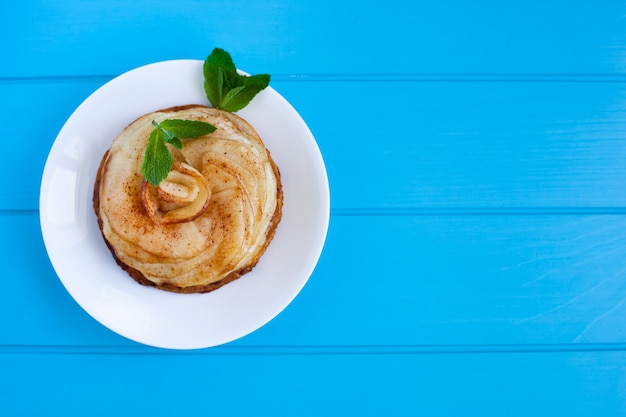 Apple pie with cinnamon and mint on a bright blue wooden background