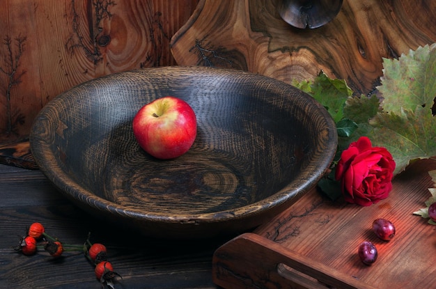 An apple and a red rose are in a bowl.