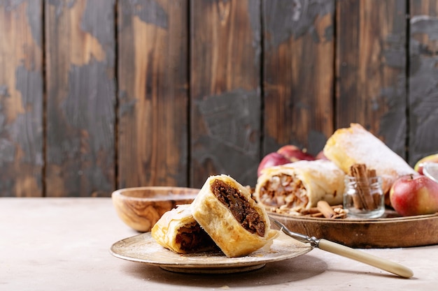 Apple strudel served with fresh apples, cinnamon sticks and walnuts over white texture background