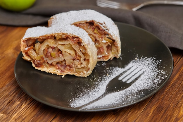 Apple strudel with icing sugar on black plate