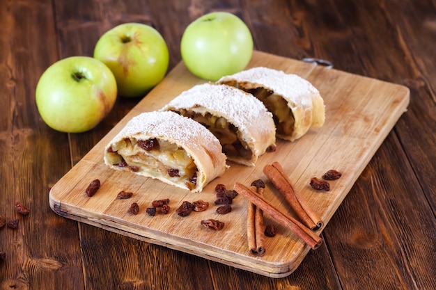 Apple strudel with icing sugar, cinnamon sticks, wooden table