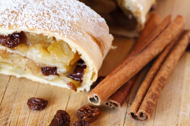 Apple strudel with icing sugar, cinnamon sticks, wooden table