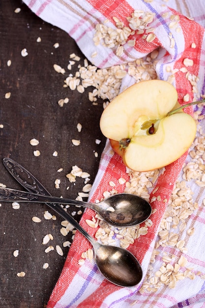 Apple with oatmeal and vintage spoons on napkin on color wooden background