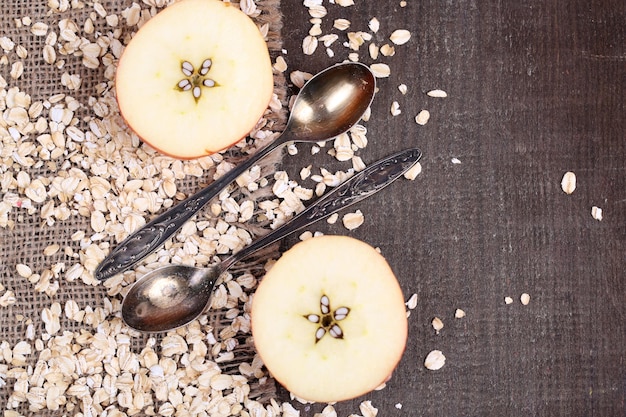 Apple with oatmeal and vintage spoons on sackcloth on color wooden background