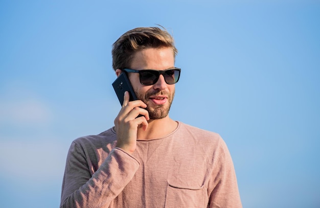 Application and internet Hipster wear sunglasses hold mobile phone sky background Hipster smartphone call Important mobile conversation Man mobile call Stay in touch Mobile call concept