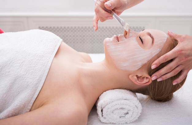 Apply face mask, spa beauty treatment and skincare. Woman getting facial nourishing mask by beautician at spa salon, close-up