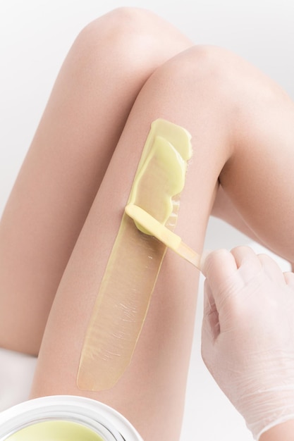 Applying hot wax on slim woman leg using spatula Professional depilation waxing in beauty salon