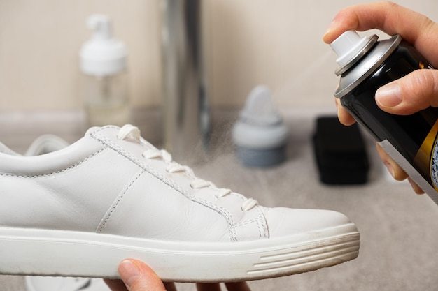 Photo applying a waterrepellent hydrophobic spray to white women's sneakers