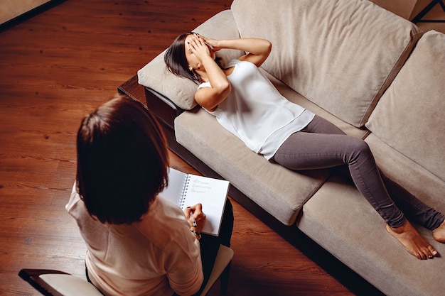 Appointment with a psychologist. Pretty adult woman lying on a sofaand covers his face with his hands in pain.