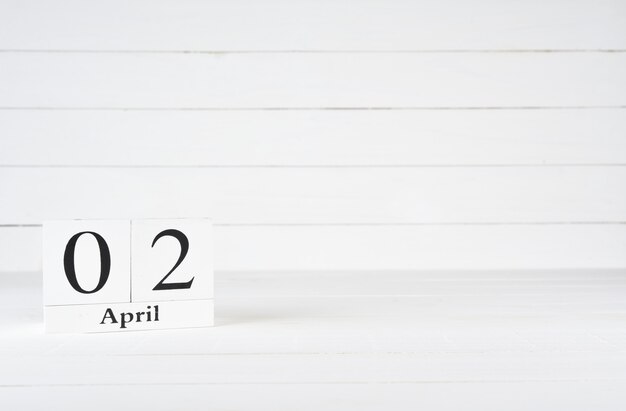 Photo april 2nd, day 2 of month, birthday, anniversary, wooden block calendar on white wooden background with copy space for text.