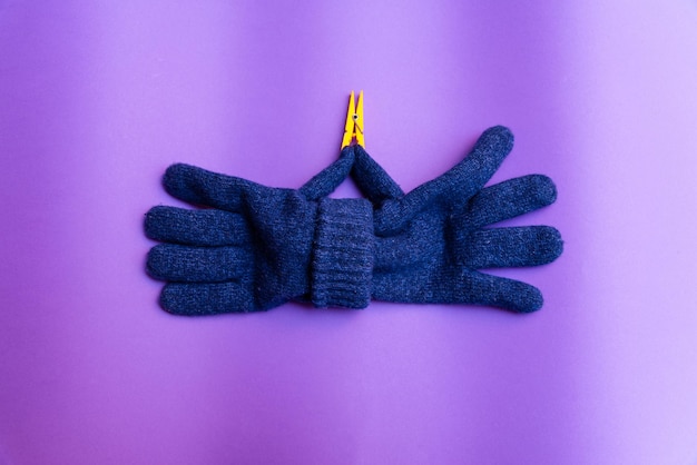 Photo april fools day concepta pair of knitted blue gloves on purple backgroundthe thumb has a laundry clip