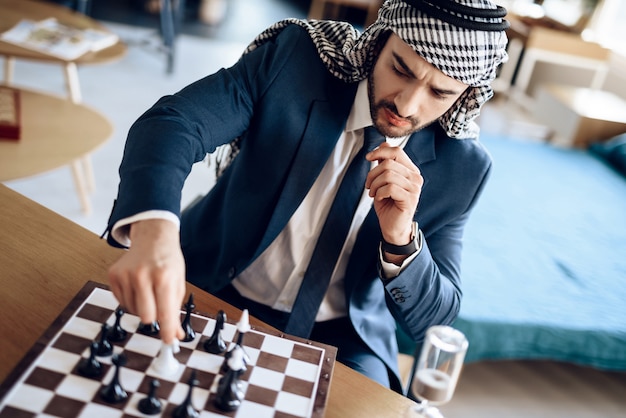 Arab businessman playing chess at table at hotel room.