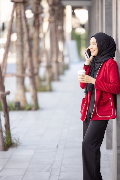 Arab businesswomen in hijab holding a coffee in the street and holding a cell phone