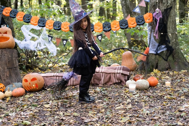 Arab girl in halloween costume and witch hat with broom in halloween decoration outdoor