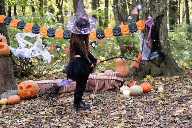 Arab girl in halloween costume and witch hat with broom in halloween decoration outdoor