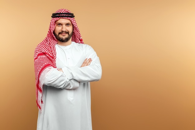 Arab man businessman in national clothes folded his arms on his chest, beige wall. 