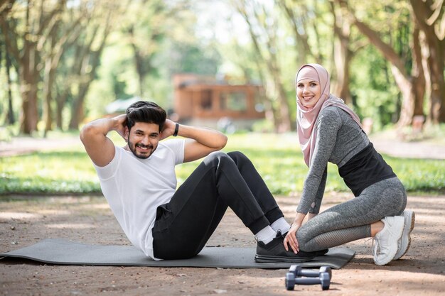 Arab man doing exercise for abs while woman holding his legs