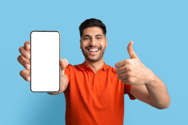 Arab man showing blank smartphone with white screen and gesturing thumb up