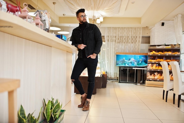 Arab man wear on black jeans jacket and eyeglasses in cafe drink coffee at bar Stylish and fashionable arabian model guy