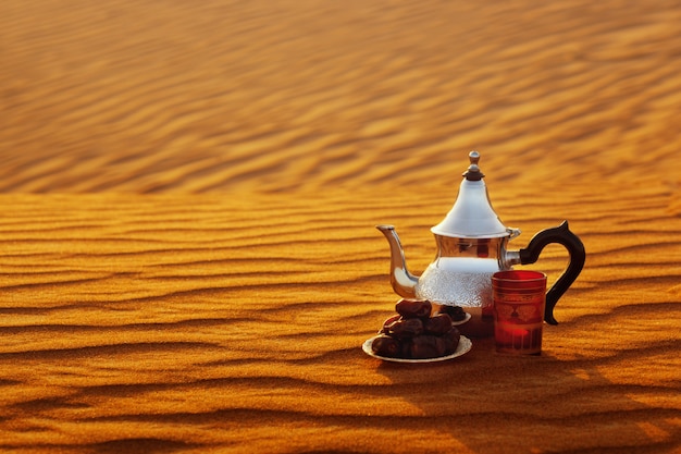 Arab teapot, cup and dates stand on the sand in the desert 