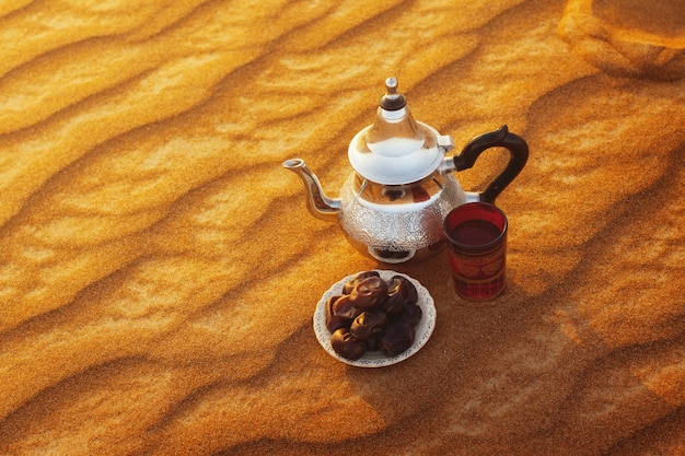 Arab teapot, cup and dates stand on the sand in the desert 