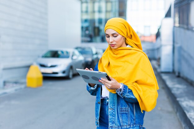 Arab woman student. Beautiful muslim female student wearing bright yellow hijab holding tablet